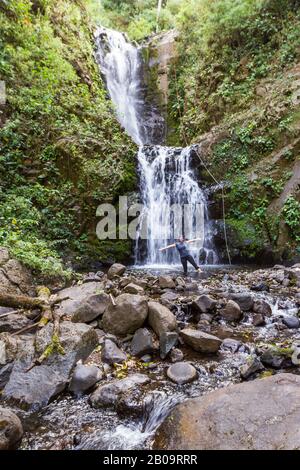 Donna locale che si trova alla base di una bella cascata nella foresta pluviale tropicale del Costa Rica Foto Stock