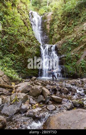 Donna locale che si trova alla base di una bella cascata nella foresta pluviale tropicale del Costa Rica Foto Stock