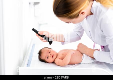 Pediatra esamina l'orecchio del bambino di 2 settimane in una nuova clinica pediatrica. Giovane medico che usa otoscopio (auriscopio) per controllare il canale uditivo e la membrana del timpano. Foto Stock