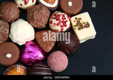 Primo piano di una selezione di cioccolatini di lusso, con un cuore rosa avvolto in lamina, che potrebbe essere per un regalo. Foto Stock