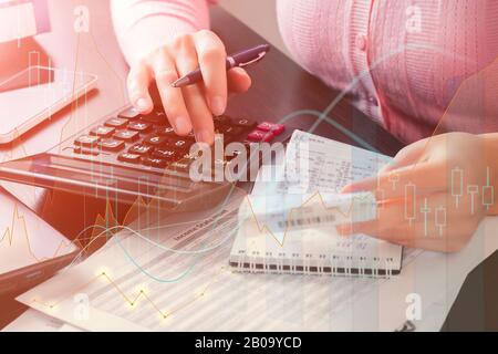 Contabile femminile in ufficio tiene in mano una ricevuta di cassa e utilizza una calcolatrice per calcolare le spese, scrive i dati ricevuti in un notebook. Foto Stock