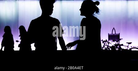 Silhouette di ragazzo e ragazza teen in piedi di fronte al moderno edificio, nella notte in alto contrasto nero e viola bianco Foto Stock