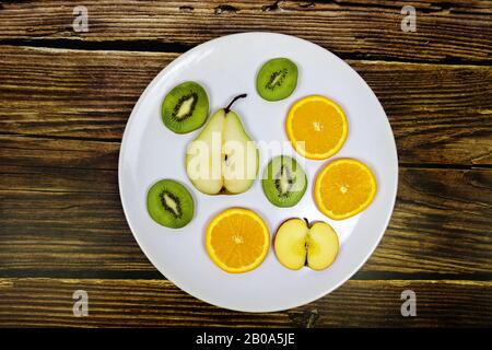 frutta a fette pera kiwi mela arancione su un piatto bianco witg rustico sfondo di legno Foto Stock