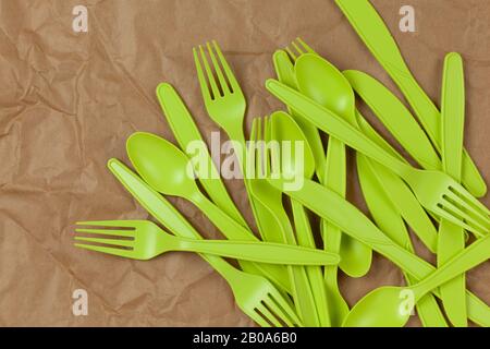 Sfondo da forcella verde riciclabile riutilizzabile, cucchiai, coltelli realizzati con amido di mais su carta da artigianato marrone sbriciolata. Eco, zero rifiuti, alternativa a p Foto Stock