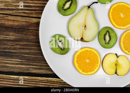 frutta a fette pera kiwi mela arancione su un piatto bianco witg rustico sfondo di legno Foto Stock