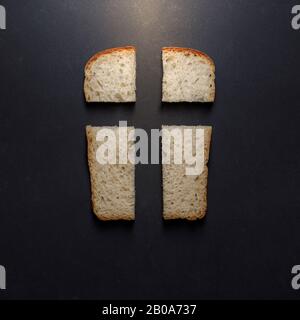 Il nostro pane quotidiano, metafora e segno. Croce, valori cristiani, concetto di religione cristiana. Pane sotto forma di croce su sfondo nero, top vie Foto Stock