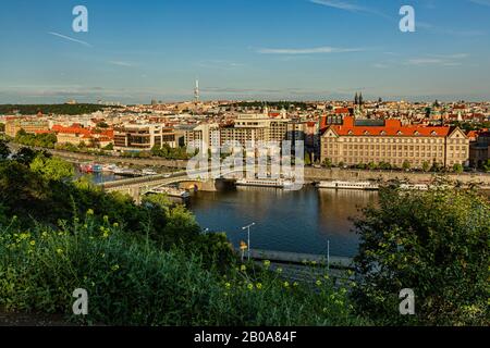 Praga / Repubblica Ceca - 23 maggio 2019: Vista panoramica del paesaggio urbano con case, Zizkov torre, fiume Moldava, ponte e barche. Cielo blu sera. Foto Stock