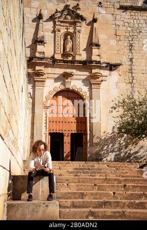 Uomo con iphone, seduto su scala, al di fuori del tempio barocco Foto Stock