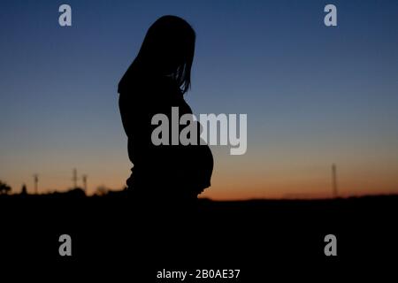 Una donna incinta è silhoueted contro un tramonto colorato Foto Stock