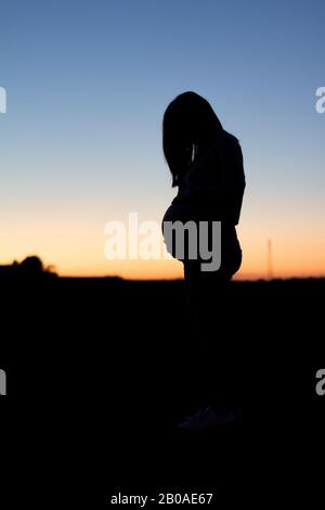 Una donna incinta è silhoueted contro un tramonto colorato Foto Stock