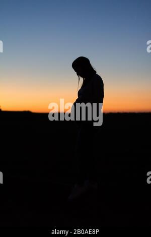 Una donna incinta è mezza silhoueted contro un tramonto colorato Foto Stock