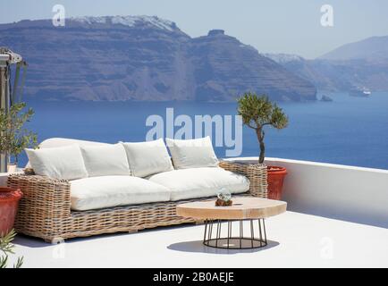 Bella terrazza con divano e un piccolo tavolo nel villaggio di Oia nell'isola greca di Santorini. Nessuno si sta godendo ora lo spettacolare panorami Foto Stock