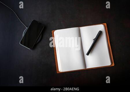 Un giornale aperto e un iPhone in ricarica wireless su una scrivania in legno. Foto Stock