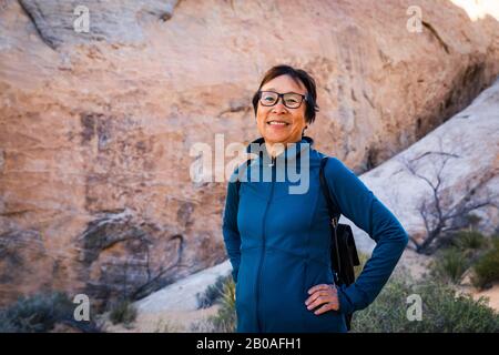 Ritratto di sorridente Senior Asian Woman escursioni nel paesaggio desertico Foto Stock