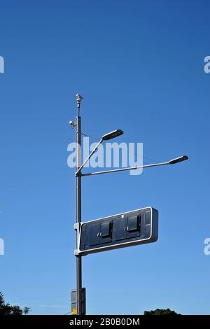 Telecamera di sicurezza su un palo di luce dell'autostrada, un cielo blu chiaro, come un insetto dell'avambraccio, due luci un segno rettangolare di informazioni, sorveglianza della strada Foto Stock