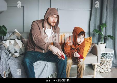 Padre e figlio Tween boy in hoodies giocare giochi per computer con joystick a casa tipica caucasica famiglia Foto Stock