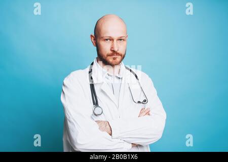 Attraente serio uomo bald bearded medico guardando la macchina fotografica isolata sullo sfondo blu Foto Stock