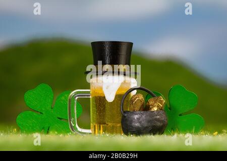 Tazza di birra color ambra, trifogli a quattro foglie e una pentola d'oro su un prato erboso all'aperto Foto Stock