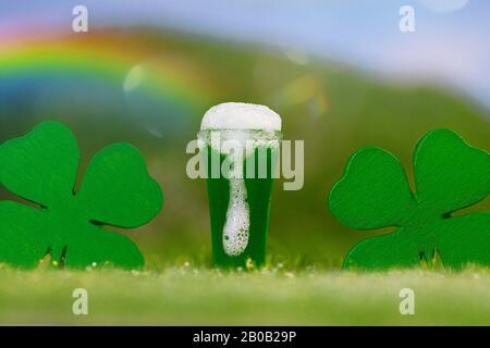 Pinta di birra verde, trifogli a quattro foglie sotto l'arcobaleno su un prato erboso, verde, all'aperto Foto Stock