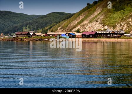 Ake Baikal vicino al villaggio di Port Baikal, Russia. Orizzontale vista giorno della costa alta, verde foresta, case, acqua lago chiaro in estate Foto Stock