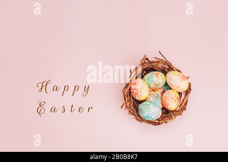 Le uova di pasqua Coloseful nel nido su sfondo di colore rosa pastello. Foto Stock