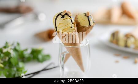 Vista ravvicinata del dessert estivo, coni gelato alla vaniglia con sciroppo di cioccolato condito in cima in sfondo sfocato Foto Stock