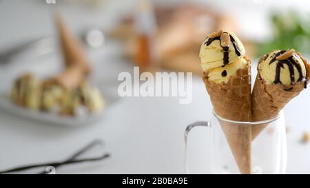 Un taglio corto di dessert estivo, coni gelato alla vaniglia con sciroppo di cioccolato condito in cima in sfondo sfocato Foto Stock
