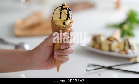 Vista ravvicinata di una ragazza che tiene il cono gelato alla vaniglia con sciroppo di cioccolato gocciolato in cima Foto Stock