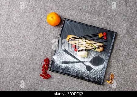 Strudel si trova su un piatto nero quadrato con una palla di gelato e lamponi. Su una tela grigia. Accanto a mandarino, ribes e noce Foto Stock