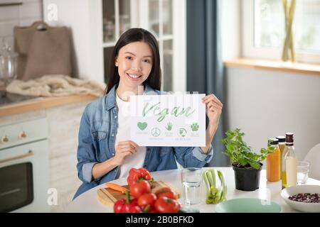 Giovane donna seduto al tavolo che tiene un poster nelle sue mani. Foto Stock