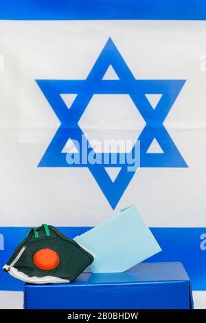 Elezioni Israele. Maschera facciale respiratoria batterica in una scatola per le elezioni in Israele sfondo bandiera. Gli israeliani messi in quarantena per il coronavirus avranno le cabine di voto per le elezioni di marzo. Foto Stock