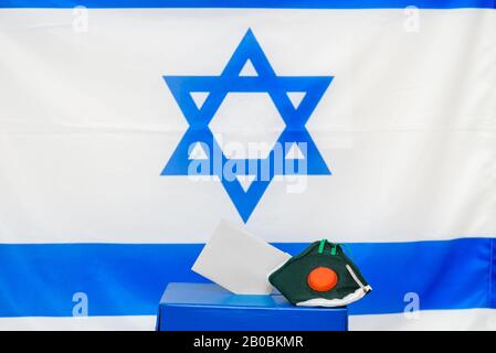 Elezioni Israele. Maschera facciale respiratoria batterica in una scatola per le elezioni in Israele sfondo bandiera. Gli israeliani messi in quarantena per il coronavirus avranno le cabine di voto per le elezioni di marzo. Foto Stock