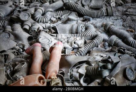 Le gambe di una bambola rotta su un mucchio di maschere a gas dell'epoca sovietica in un edificio abbandonato a Pripyat, in Ucraina, dove si trova il desaster nucleare di Cernobyl del 1986. Foto Stock