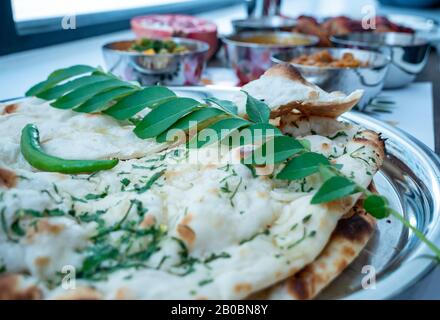 Primo piano di una selezione di piatti thali indiani. Alcuni pane naan appena appoggiato sedersi in primo piano guarnito con alcune foglie di curry e verde c Foto Stock