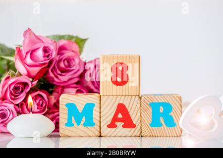 Calendario Internazionale della Giornata della Donna sfondo biglietto d'auguri. Con cuore di legno, rilassante candela a fuoco e bouquet decorativo rosa rosa sullo sfondo. Foto Stock