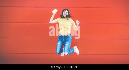 Ragazza pazzi asiatica che salta e ascolta la musica all'aperto - felice donna cinese che celebra e balla al di fuori - Divertimento, generazione millenaria e tecnologia Foto Stock