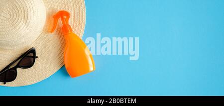 Bottiglia spray solare, cappello da spiaggia femminile e occhiali da sole isolati su sfondo blu. Protezione solare e prodotti cosmetici solari. Piatto, superiore Foto Stock