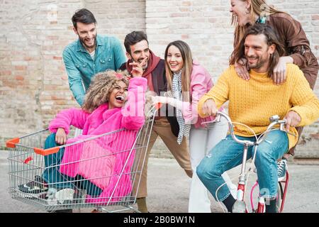 Giovani alla moda che corrono con shopping kart e bicicletta d'epoca - amici pazzi Felici divertirsi insieme all'aperto nel centro - la vita dei giovani Foto Stock