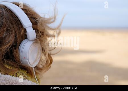persona matura che indossa le cuffie per ascoltare la musica al mare, nel nord di norfolk, inghilterra Foto Stock