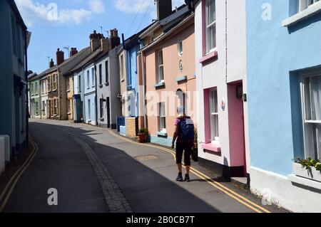 Donna Hiker camminare lungo Irsha Street una Stretta strada di Color Pastello Case Terrazzate in Appledore sul South West Coast Path. Devon Nord. Foto Stock