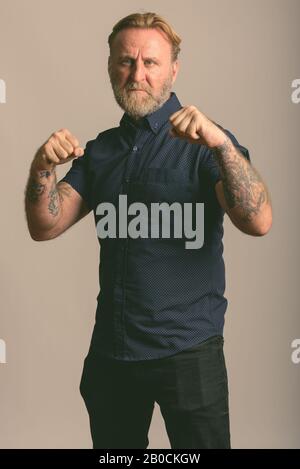 Studio shot maturo di uomo barbuto con la mano i tatuaggi tenetevi pronti a combattere in uno sfondo grigio Foto Stock