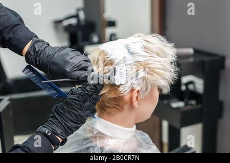 Il parrucchiere applica il colorante bianco sui capelli della donna nel salone di bellezza. Foto Stock