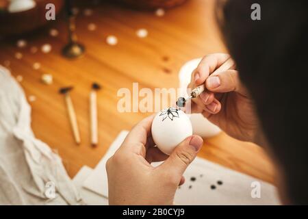 Mani pittura uovo di pasqua con cera calda sullo sfondo di tavola di legno. Moderne uova di Pasqua con eleganti ornamenti in cera. Buona Pasqua. Zero sprechi. Ucraino Foto Stock