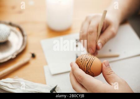 Mani pittura uovo di pasqua con cera calda sullo sfondo di tavola di legno. Moderne uova di Pasqua con eleganti ornamenti in cera. Buona Pasqua. Zero sprechi. Ucraino Foto Stock