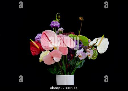 Bouquet di fiori colorati con fiori di Flamingo rosso e bianco, viola Lisianthus o Eustoma, Orchid e arrotolato felce isolato su sfondo nero Foto Stock