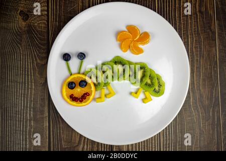 divertente verme di frutta su piatto bianco dolce sano per i bambini su tavola di legno . Foto Stock