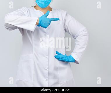 donna medic in camice bianco con bottoni sulle mani, indossando guanti sterili blu, con gesto della mano che indica il soggetto, sfondo bianco Foto Stock