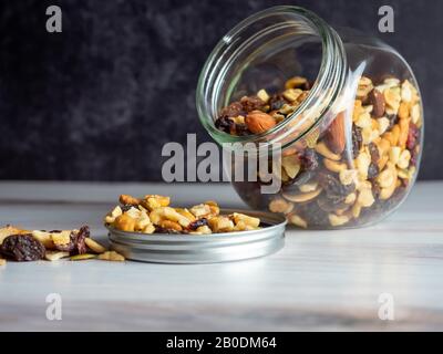 Vaso di vetro riempito con noci sane e frutta secca che fuoriesce su una superficie di legno con uno sfondo di ardesia nera. Grassi sani e carbs. Foto Stock