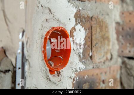 Presa di caselle di colore arancione con i fili in una parete. Installazione del cablaggio di fili elettrici che fuoriescono dalle prese elettriche foro sulla parete di mattoni. Foto Stock