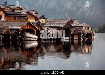 Fila di vecchie barche di legno getta nell'acqua sul lago presto la mattina. Halstatt Austria Foto Stock